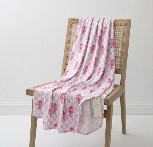 Baby wrapped in Seahorse Splash bamboo blanket featuring lavender checkered and coral seahorse print for cozy swaddle