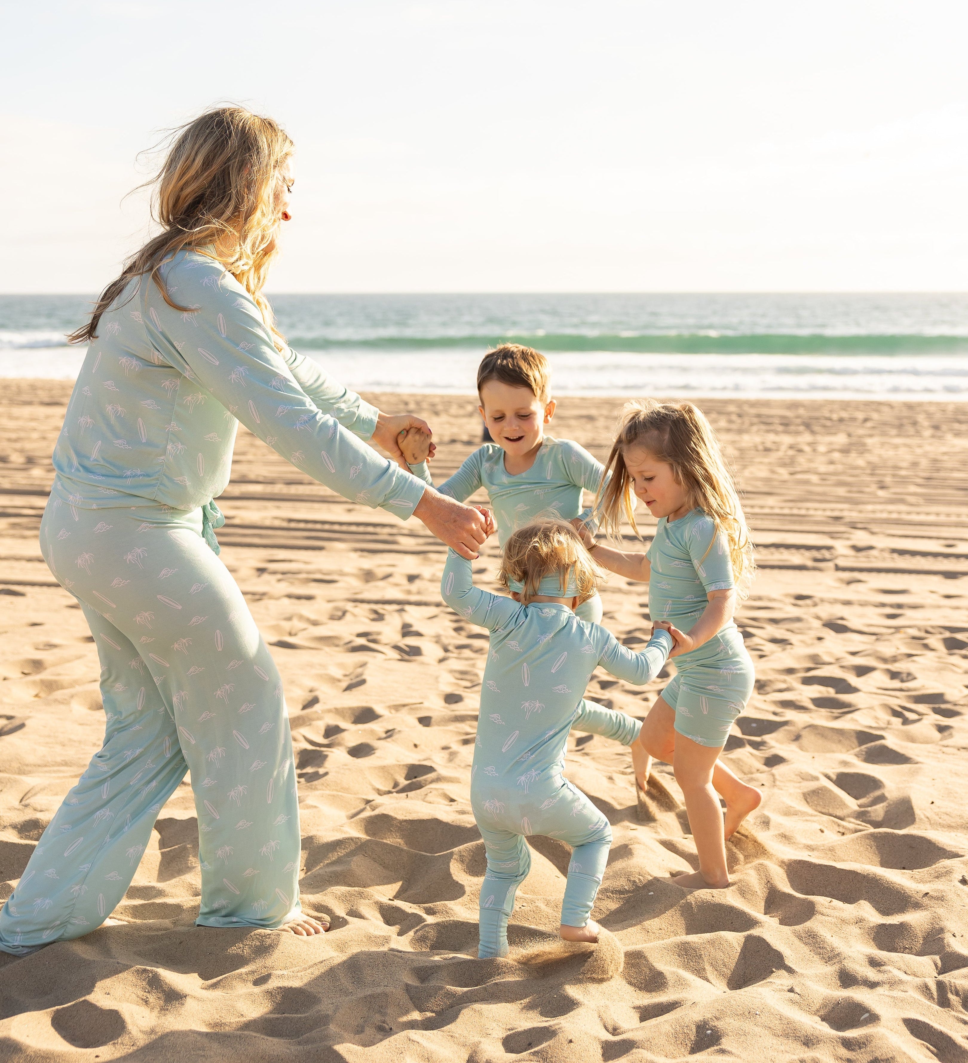 Mom and kids playing on the beach wearing matching Surfside Dreams bamboo pajamas by Shae & Palmer