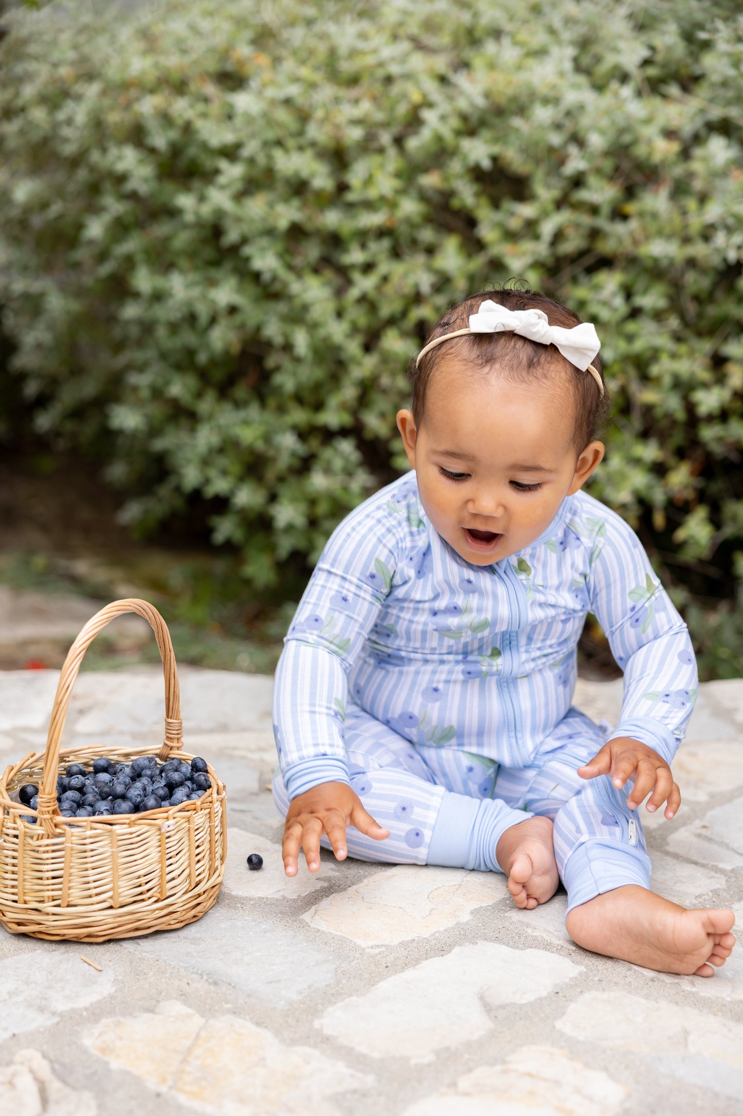 Baby wearing Blueberry Lane blue striped bamboo zip pajamas sitting beside a basket of blueberries, part of Shae & Palmer's Market Fresh collection.