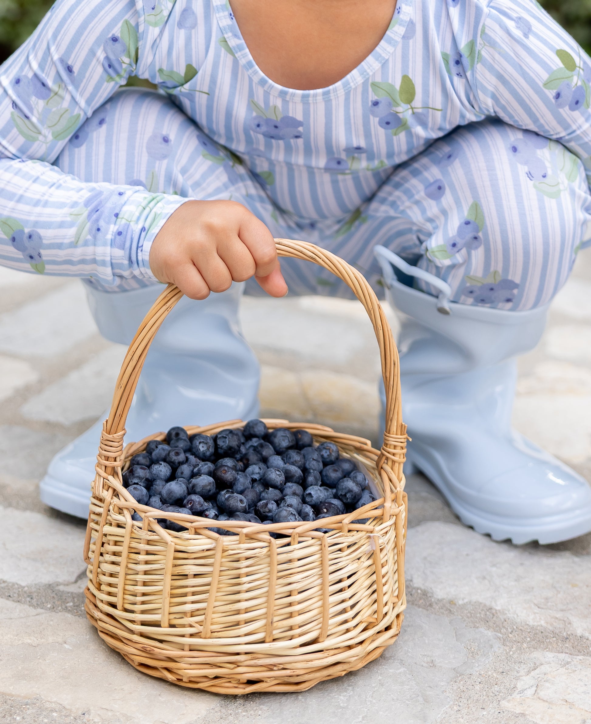 Big kid in Blueberry Lane blue striped bamboo pajamas holding a basket of fresh blueberries, part of Shae & Palmer's Market Fresh collection.