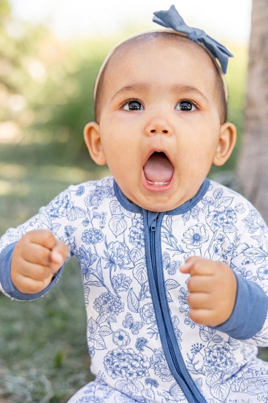 Baby wearing Shae & Palmer Botanical Blue bamboo romper featuring an elegant blue floral print, double zipper closure, fold-over footies, and ultra-soft breathable bamboo fabric.