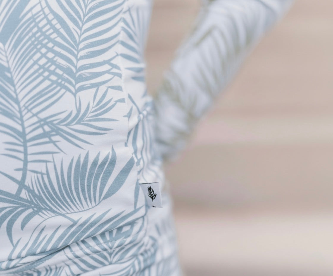 Baby wearing Cali Coastal Baby Blue bamboo romper with palm leaf print, soft breathable baby pajamas designed for comfort and everyday wear