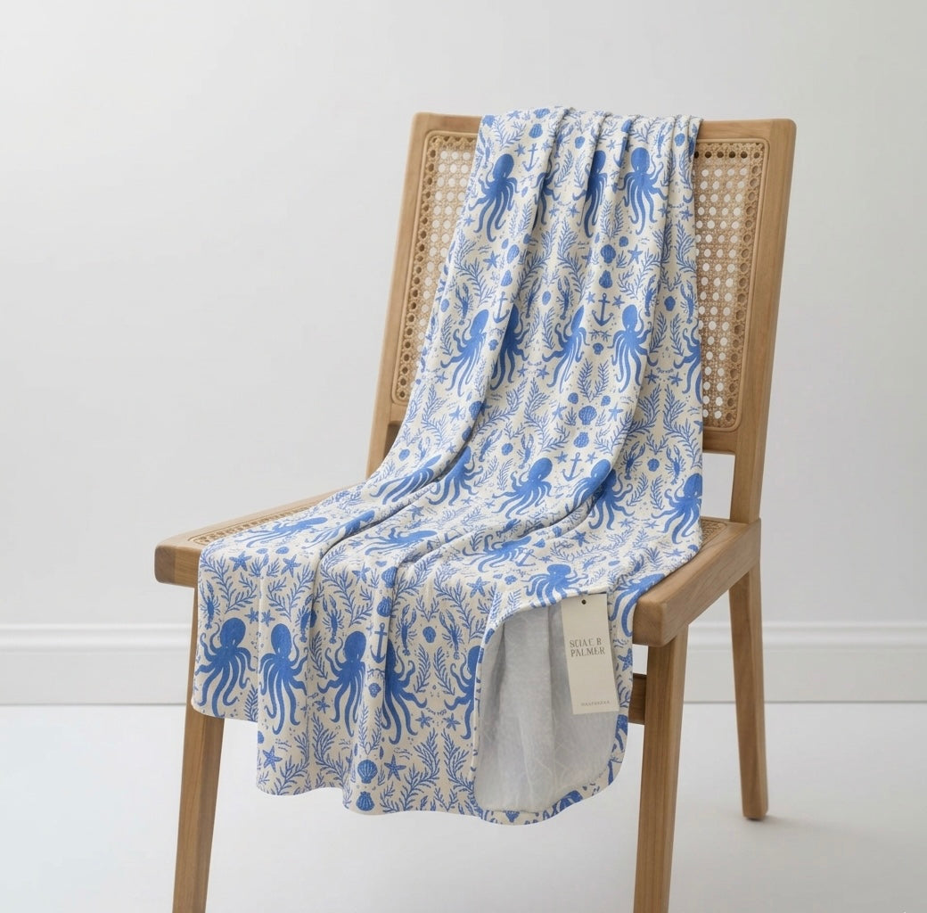 Hidden Ocean Treasures bamboo baby blanket in ocean blue with octopus, anchors, and seashell print, corner folded to show soft white underside.