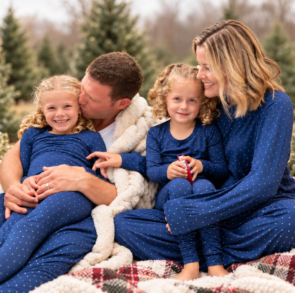 Family wearing matching Midnight Dot blue bamboo Christmas pajamas by Shae & Palmer at a holiday tree farm.