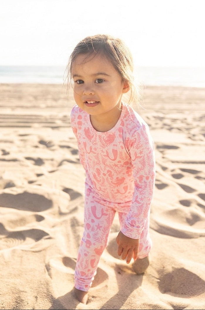 Toddler girl wearing Shae & Palmer Mermaid Cove bamboo pajamas in soft blush pink with mermaids, seashells, and starfish print