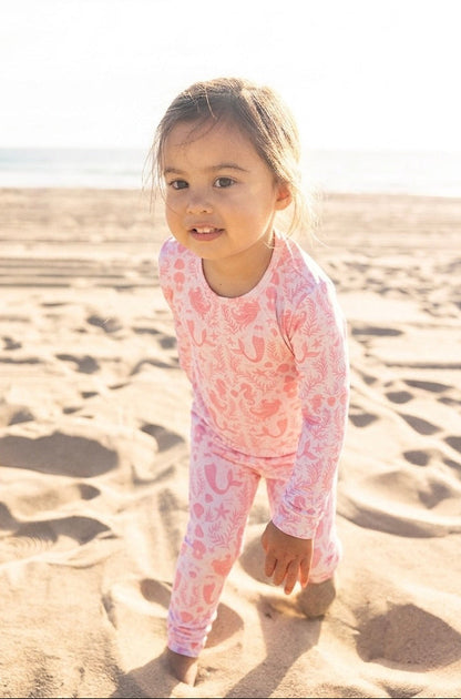 Toddler girl wearing Shae & Palmer Mermaid Cove bamboo pajamas in soft blush pink with mermaids, seashells, and starfish print
