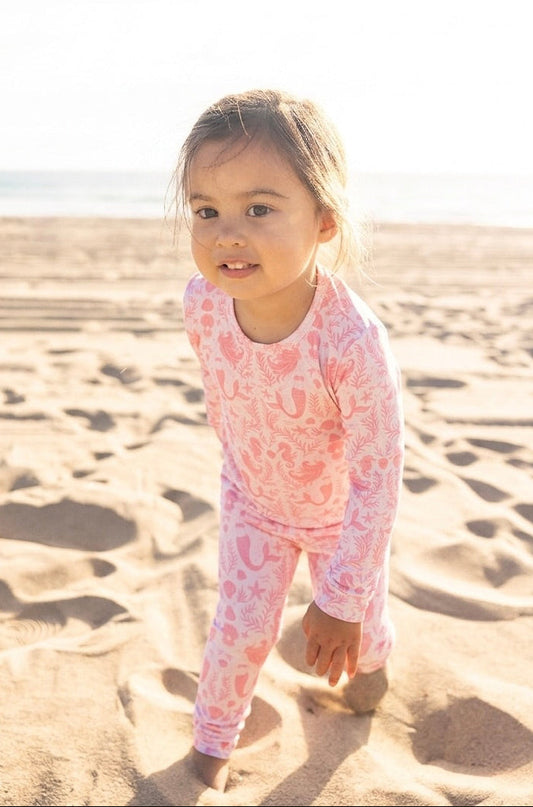 Toddler girl wearing Shae & Palmer Mermaid Cove bamboo pajamas in soft blush pink with mermaids, seashells, and starfish print