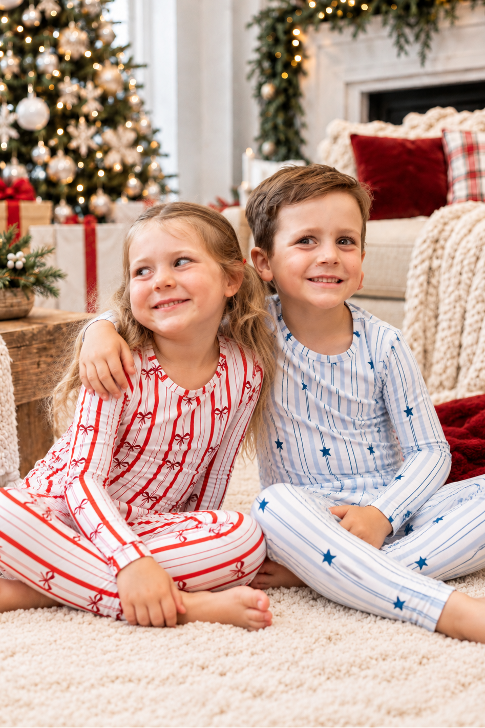 Brother and sister in matching holiday bamboo pajamas, wearing North Star blue star pajamas and Ribbon Stripe red bow pajamas