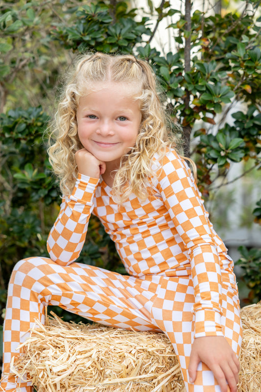 Toddler wearing Pumpkin Patch orange and ivory checkered bamboo pajamas.