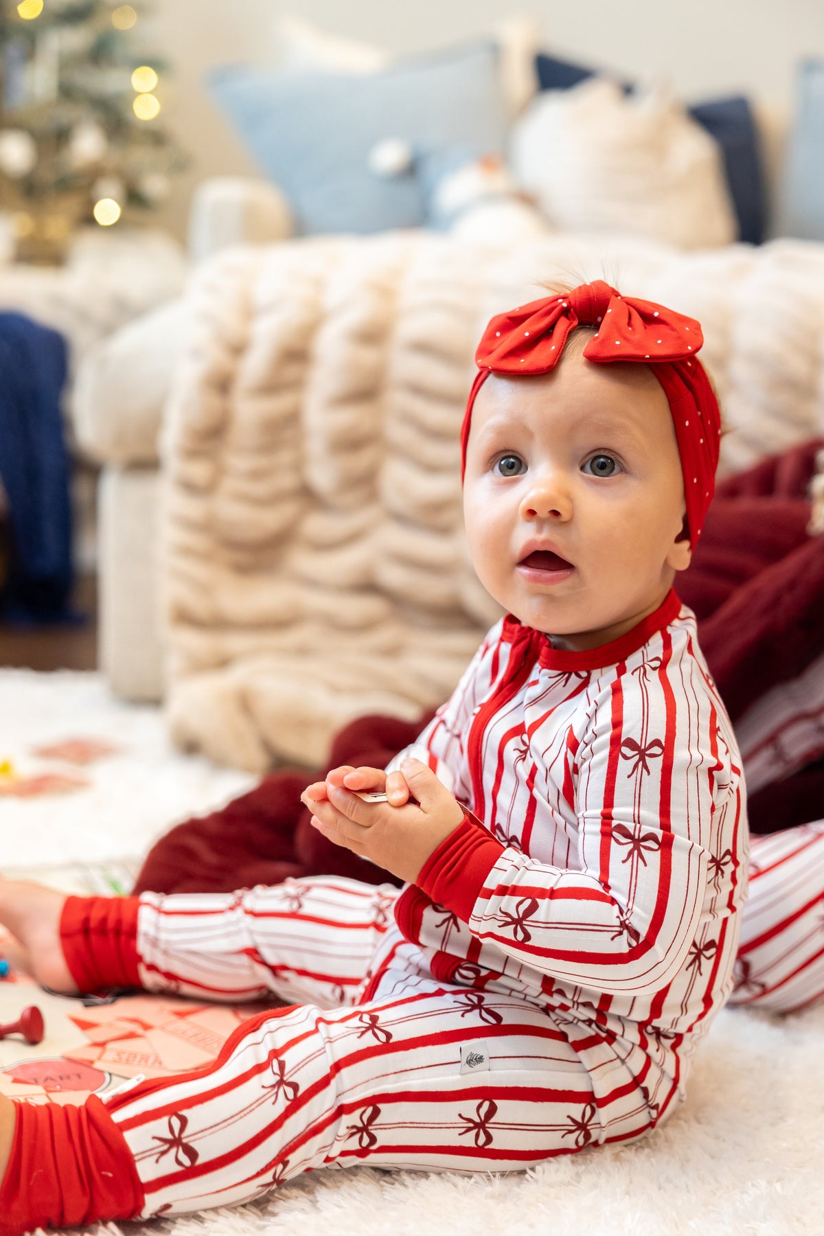 Baby wearing Ribbon Stripe bamboo pajamas by Shae & Palmer featuring classic red and white stripes with delicate bows. Soft, breathable Christmas baby pajamas perfect for matching family holiday sets, Christmas morning, festive photos, and cozy winter nights.