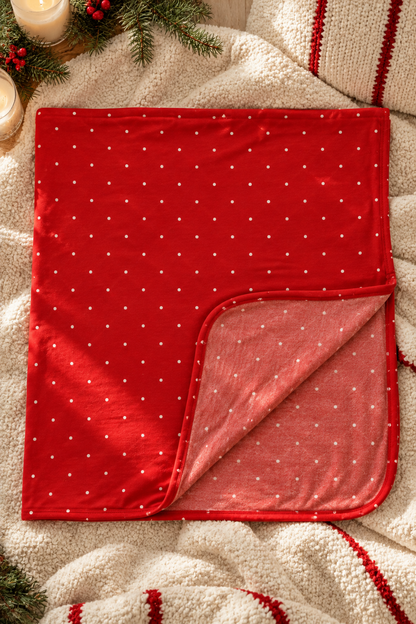 Shae & Palmer Ruby Dot red bamboo baby blanket with white polka dots styled in a cozy holiday flat lay with winter greenery and cream knits.