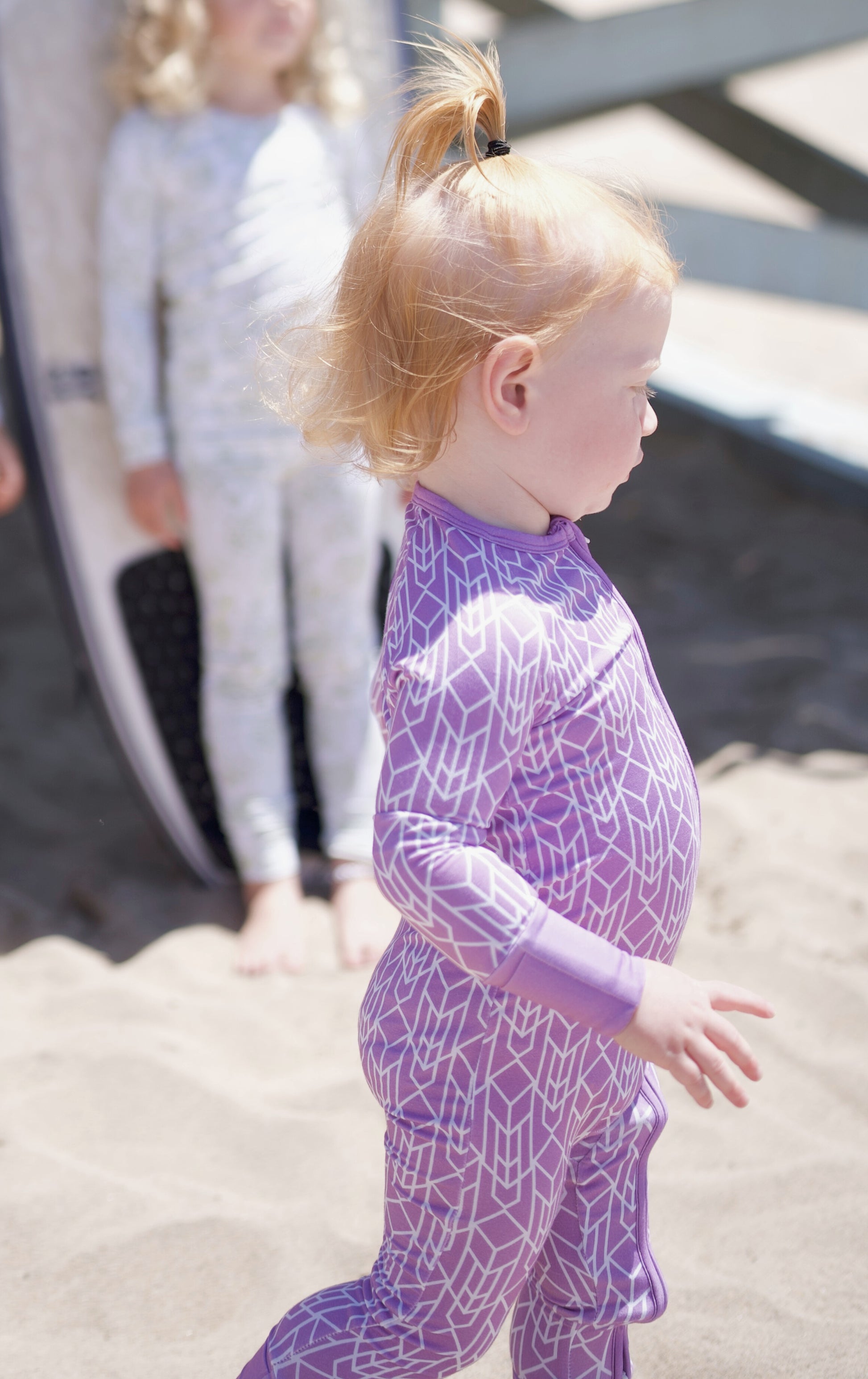 Shae & Palmer Runway Collection, bamboo baby zip romper in bold purple geometric print. Ultra-soft, breathable zip-up pajamas with double zipper for easy diaper changes and all-day comfort.