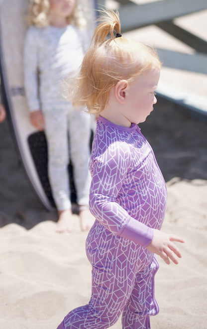 Shae & Palmer Runway Collection, bamboo baby zip romper in bold purple geometric print. Ultra-soft, breathable zip-up pajamas with double zipper for easy diaper changes and all-day comfort.