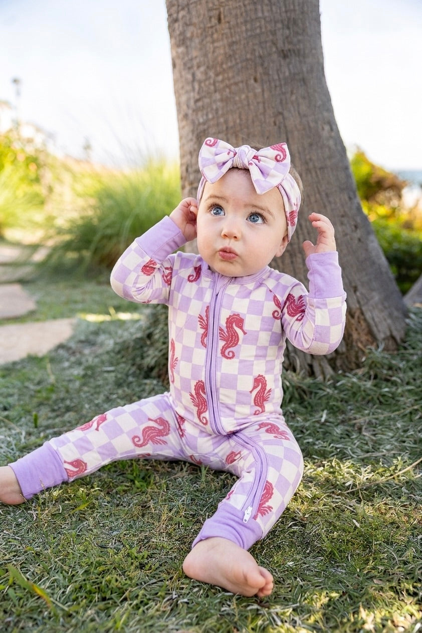 Baby wearing Shae & Palmer Seahorse Splash bamboo romper featuring playful coral seahorses on a soft lavender checkerboard print with ultra-soft breathable bamboo fabric and double zipper closure.