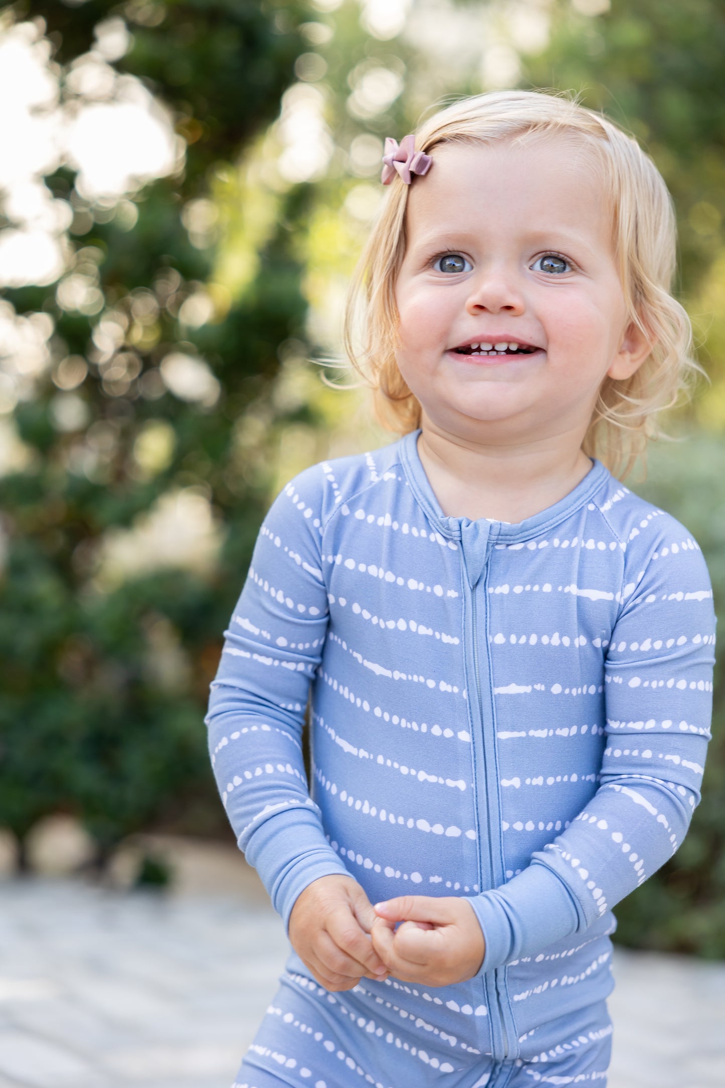 Toddler girl smiling in Blue Raspberry Stripe bamboo zip romper outdoors