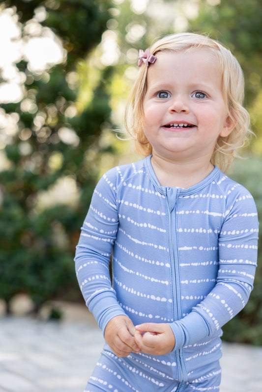 Toddler girl smiling in Blue Raspberry Stripe bamboo zip romper outdoors