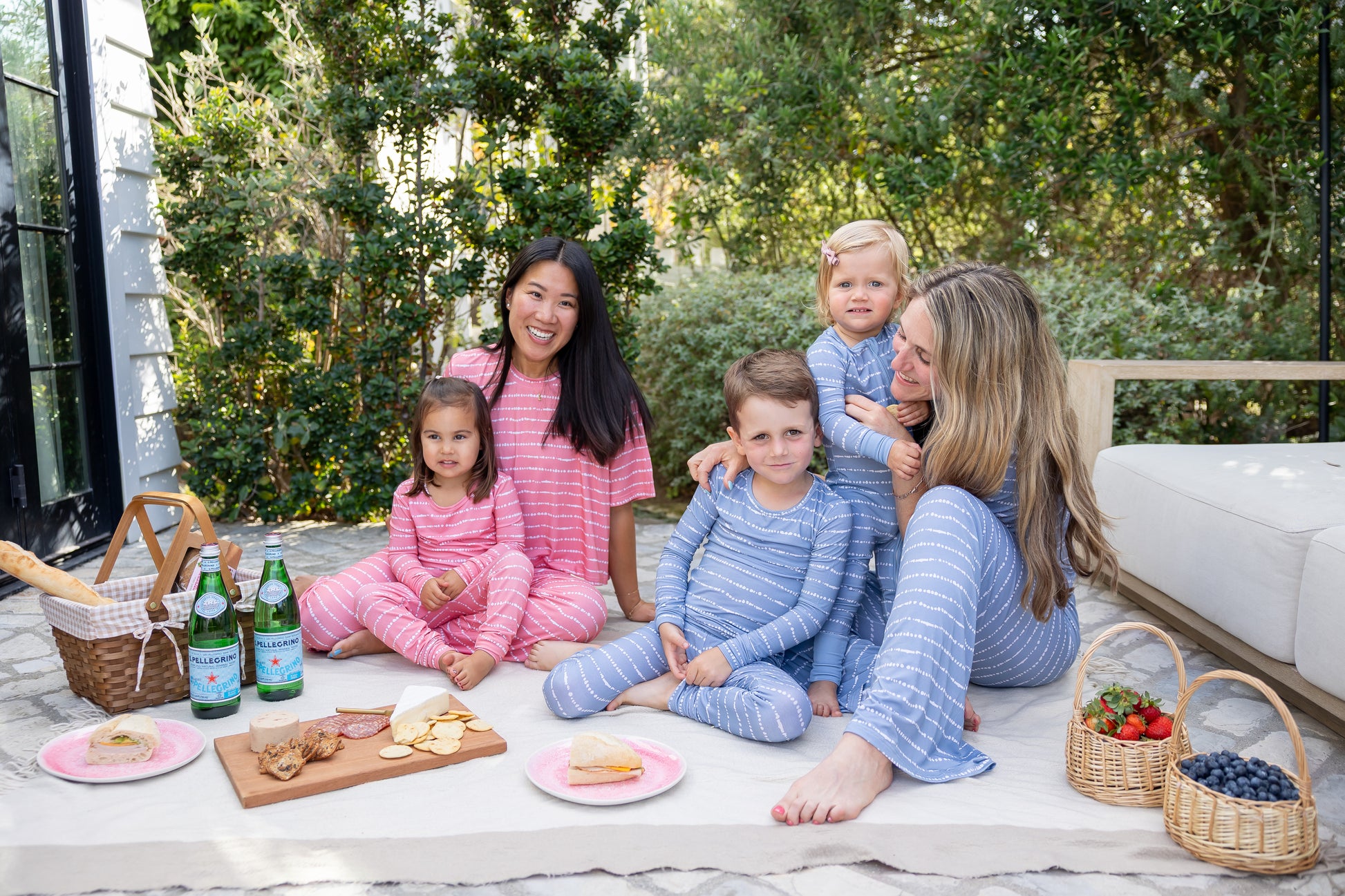 Moms and kids in matching Watermelon Blush Stripe bamboo pajamas at a backyard picnic