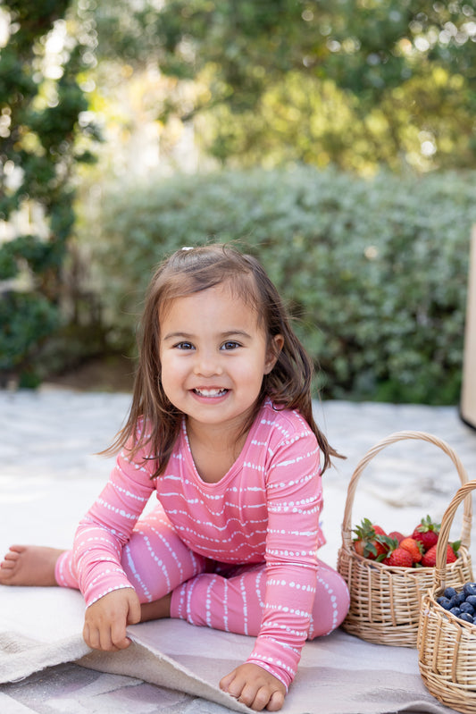 Toddler girl smiling in Watermelon Blush Stripe bamboo pajamas with berry baskets outdoors